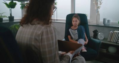 A woman listens to a girl in a therapy session.