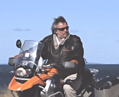 Man riding an orange BMW motorcycle near the coast.