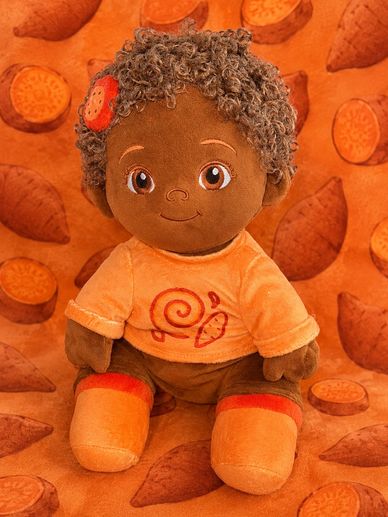 A cute plush doll with curly hair and an orange outfit sits against a sweet potato-themed background.
