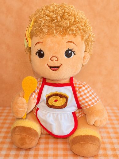 A cute plush doll with curly hair holding a yellow spoon.