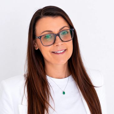 Smiling woman with long brown hair and glasses in white attire.