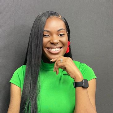 Smiling woman in a green top with long black hair and red earrings.