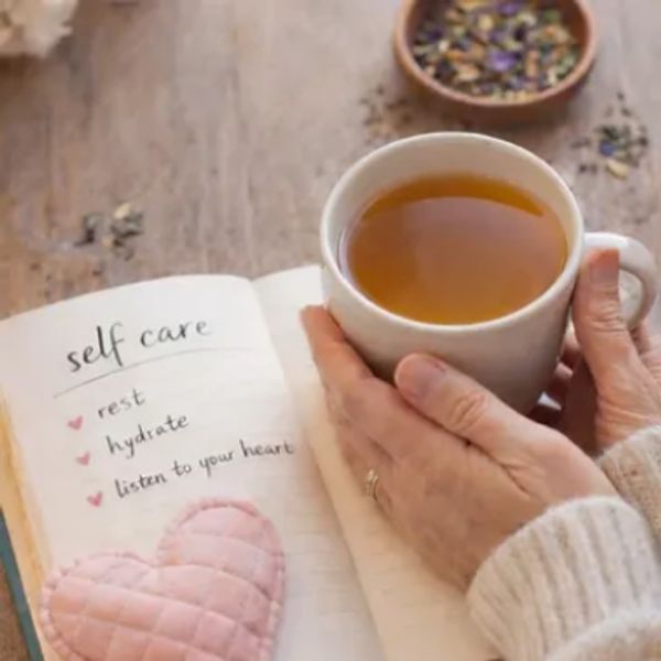 A person holding a cup of tea next to a self-care journal with reminders.