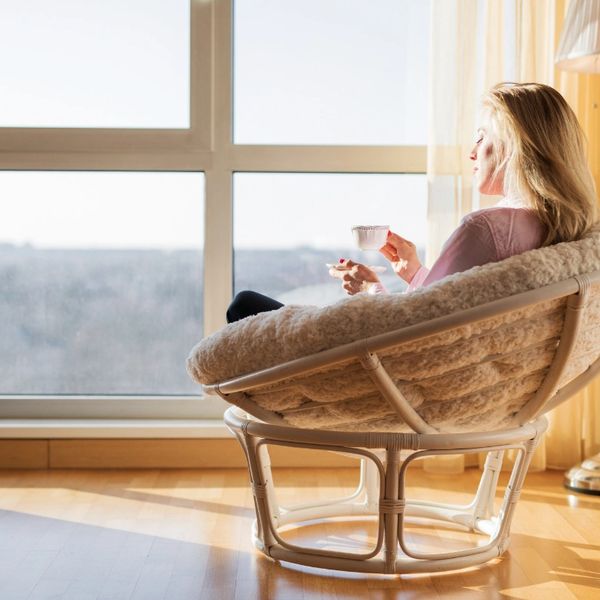 Woman relaxing in a cozy chair by a large window, enjoying a cup of tea.