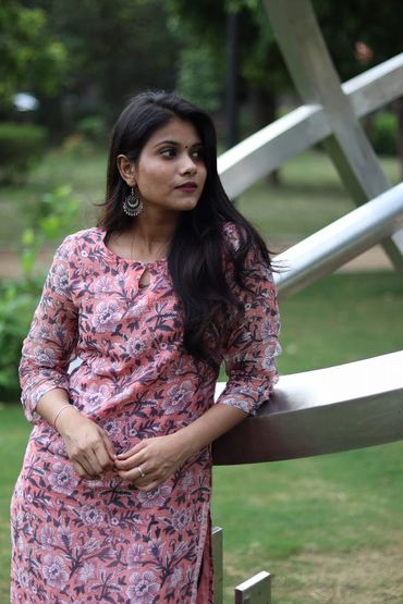 Woman in a floral dress leaning on a metallic structure outdoors.