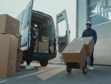 Two workers unloading packages from a delivery van using a hand truck.