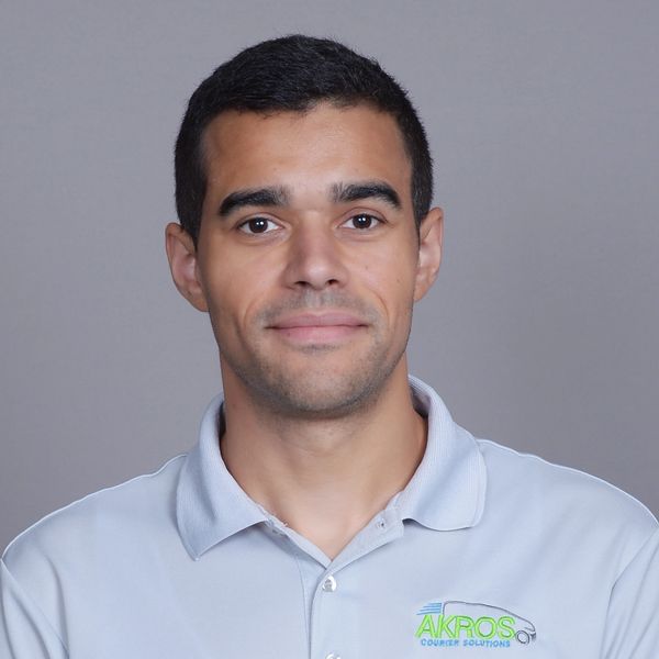 Man wearing a light gray polo shirt with company logo on a gray background.