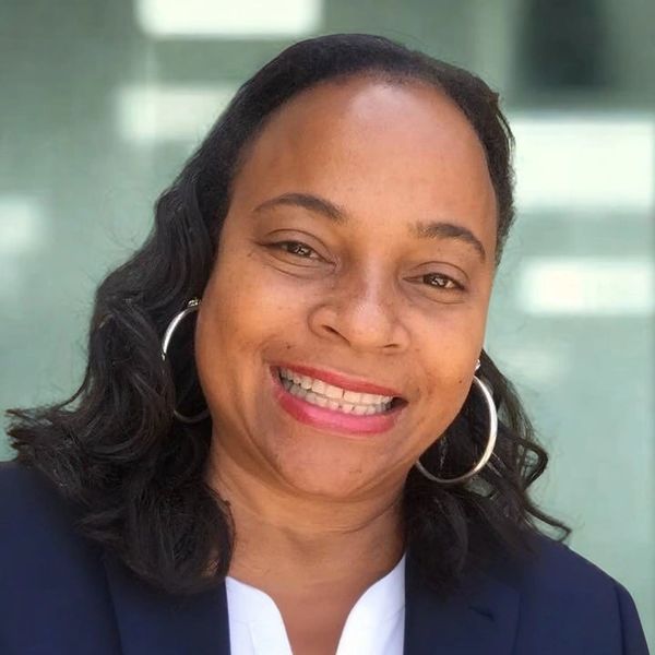 Smiling woman with hoop earrings and wavy hair in professional attire.