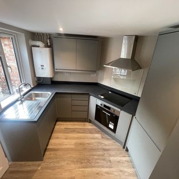 Modern grey kitchen with black countertops and wooden floor.
