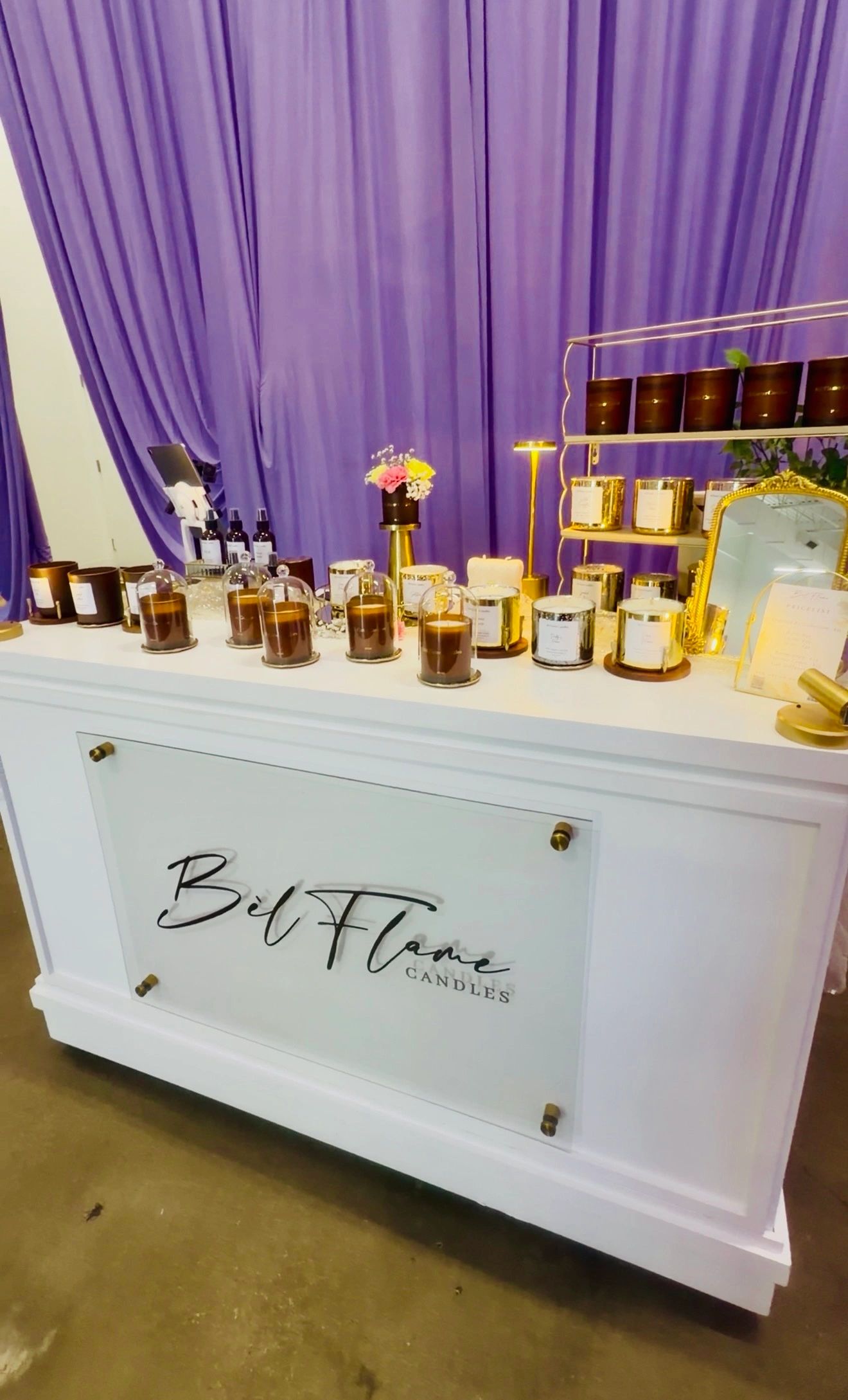 Elegant candle display on a white counter with a purple curtain backdrop.