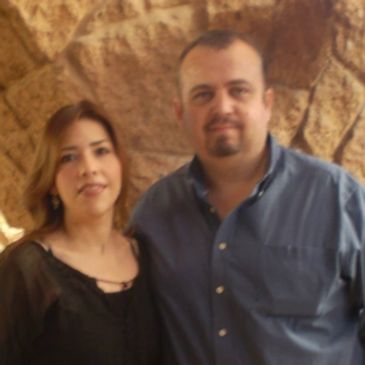 A man and woman posing together in front of a stone wall.