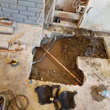 Construction site with exposed pipes and muddy water inside a dug hole.