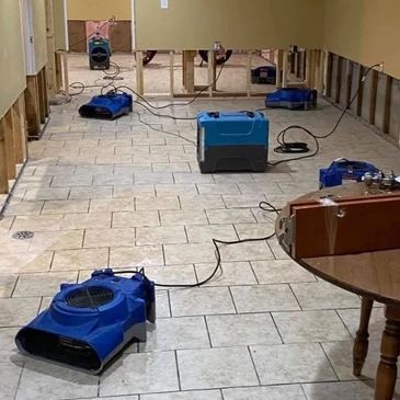 Blue air movers drying tiled floor in a partially gutted room.