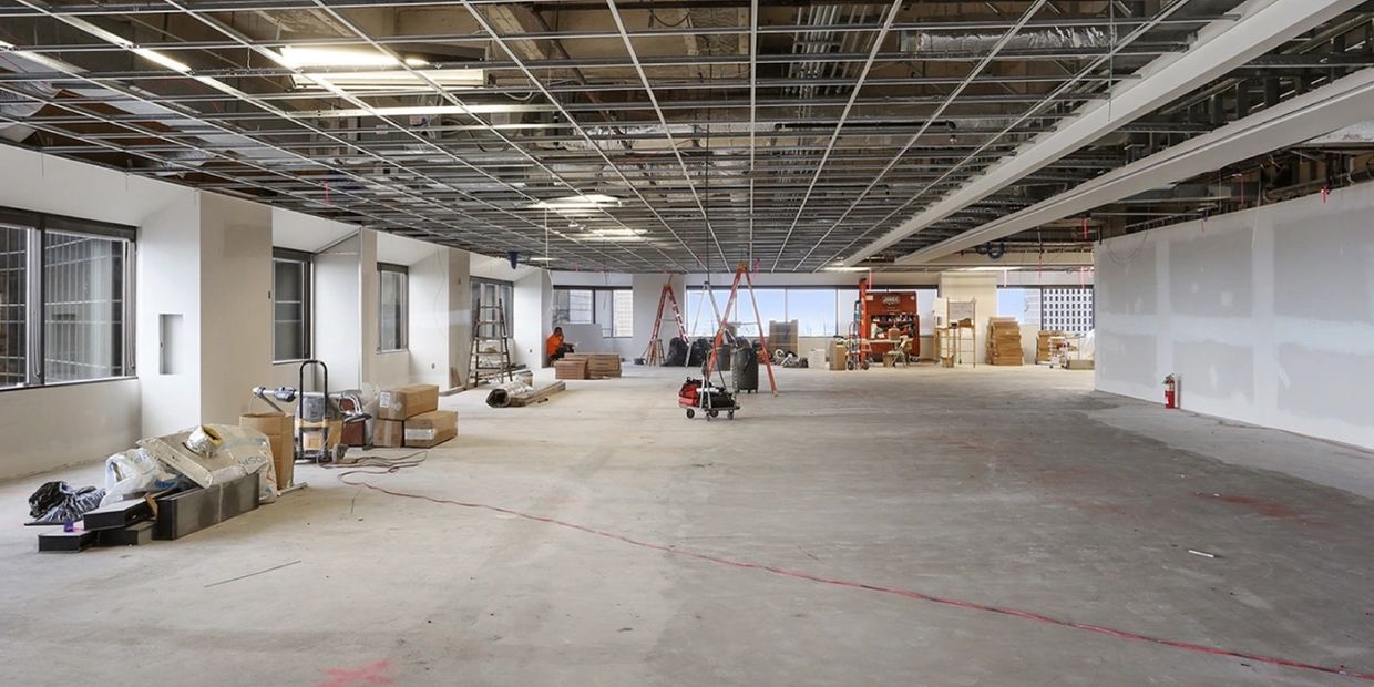 Spacious commercial interior under construction with scattered equipment and ladders.