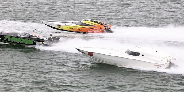 Three speedboats racing on water, creating white spray.