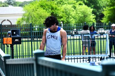 Athlete in CNU uniform preparing at an outdoor track event.