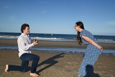 Man proposes to woman on a beach under a clear sky.
