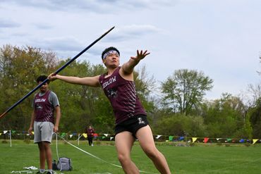 Athlete in maroon uniform preparing to throw a javelin on a grassy field.