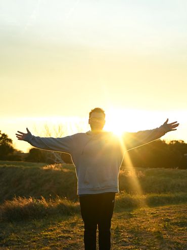 Person with arms outstretched facing the sunset in a field.