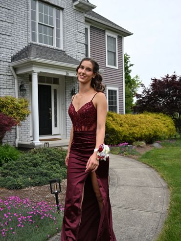 Young woman in a burgundy gown posing outside a house.