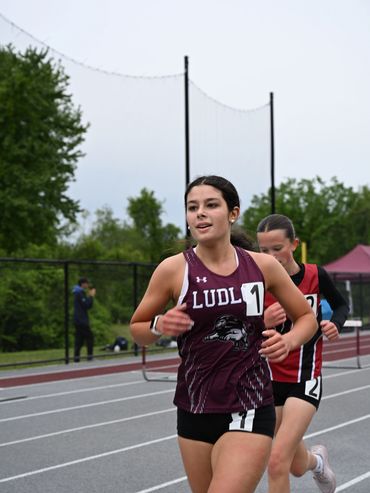 Female athlete in maroon running a track race, leading with a confident expression.