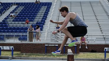 Athlete mid-jump during a track and field hurdle event in an empty stadium.