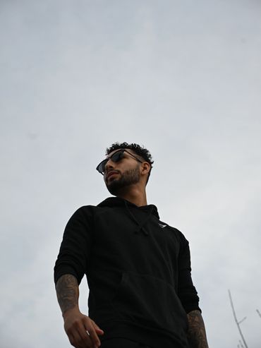 Young man in black hoodie and sunglasses looking away under cloudy sky.