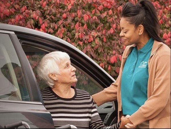 Caregiver helping elderly woman out of car with warmth and support.