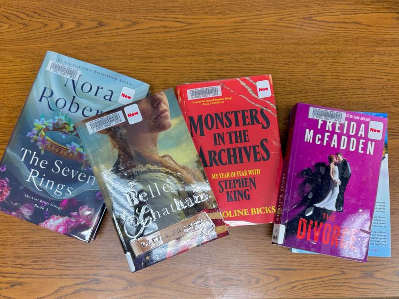 Four library books with 'New' stickers on a wooden table.