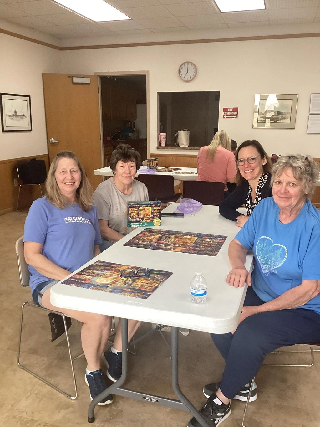 Four women sitting around a table with puzzles in a community room.
