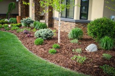 Neatly landscaped garden bed with mulch and various shrubs beside a house.