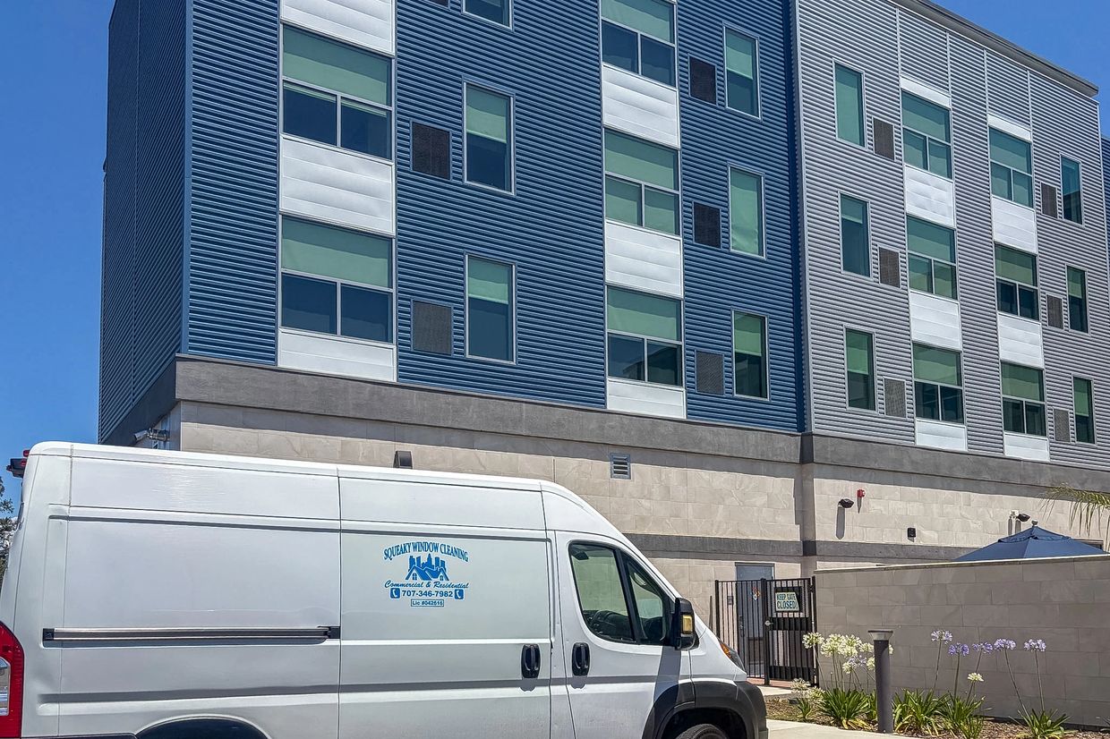 White van parked outside a modern blue and white building on a clear day.