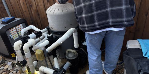 Person inspecting a complex pool pump system with multiple pvc pipes.