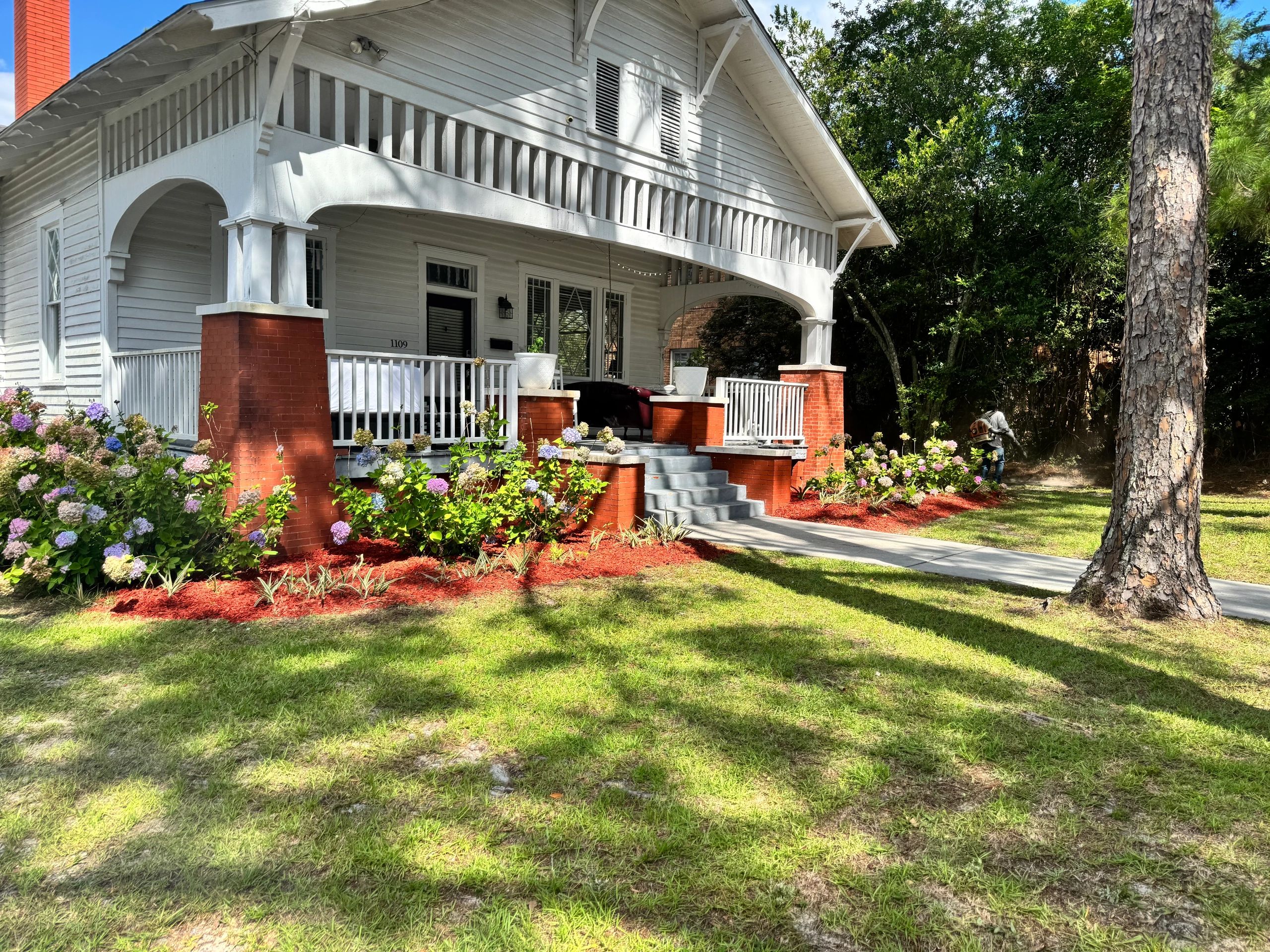 White house with red brick porch and blooming garden under sunlight.