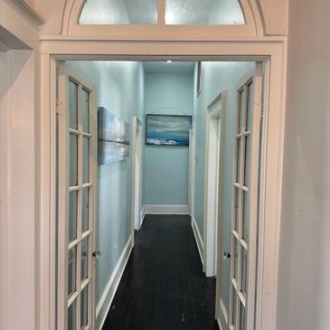 Empty hallway with light blue walls and dark flooring, featuring a framed picture at the end.