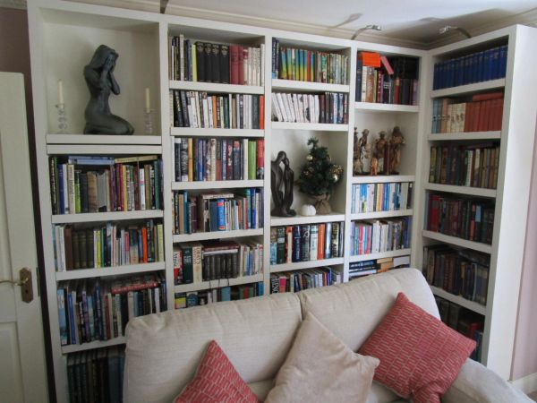 A cozy living room with a large white bookshelf and a beige sofa with red and beige cushions.