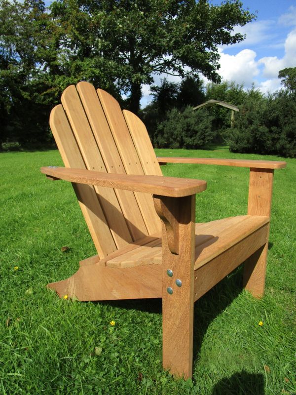Wooden Adirondack chair on green grass under a blue sky.