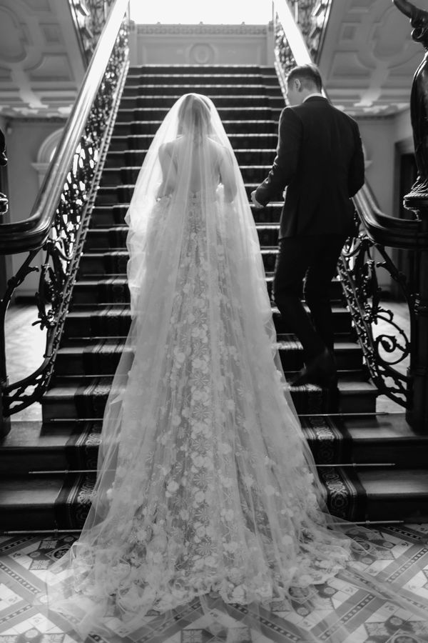 Bride and groom on grand staircase. Bride wears a wedding dress with a long train that trails behind