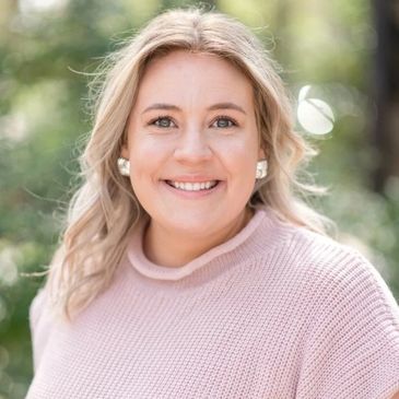 Smiling woman in a pink sweater outdoors with blurred greenery background.