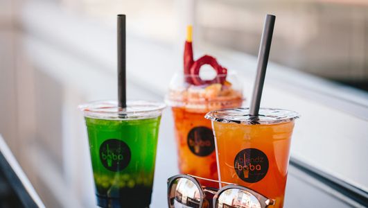 Three colorful boba drinks with straws on a table beside sunglasses.
