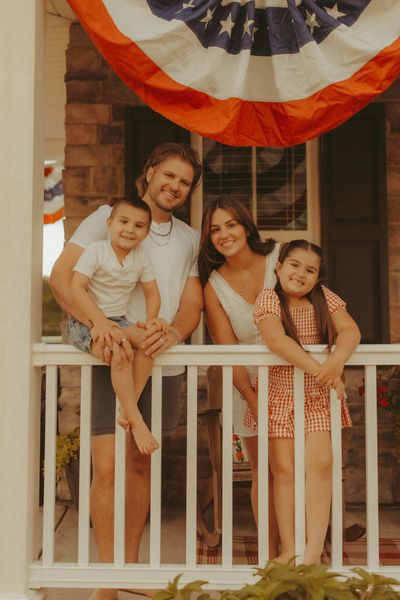 A happy family of four posing on their porch with patriotic decorations.