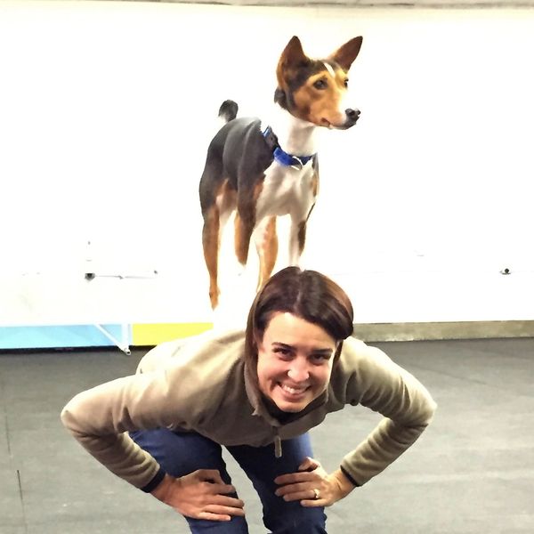 A woman with her Basenji performing a trick by balancing on her back.