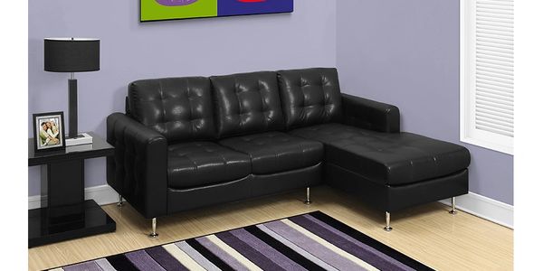 Black leather upholstered sofa with chrome legs sitting in the corner of a room.