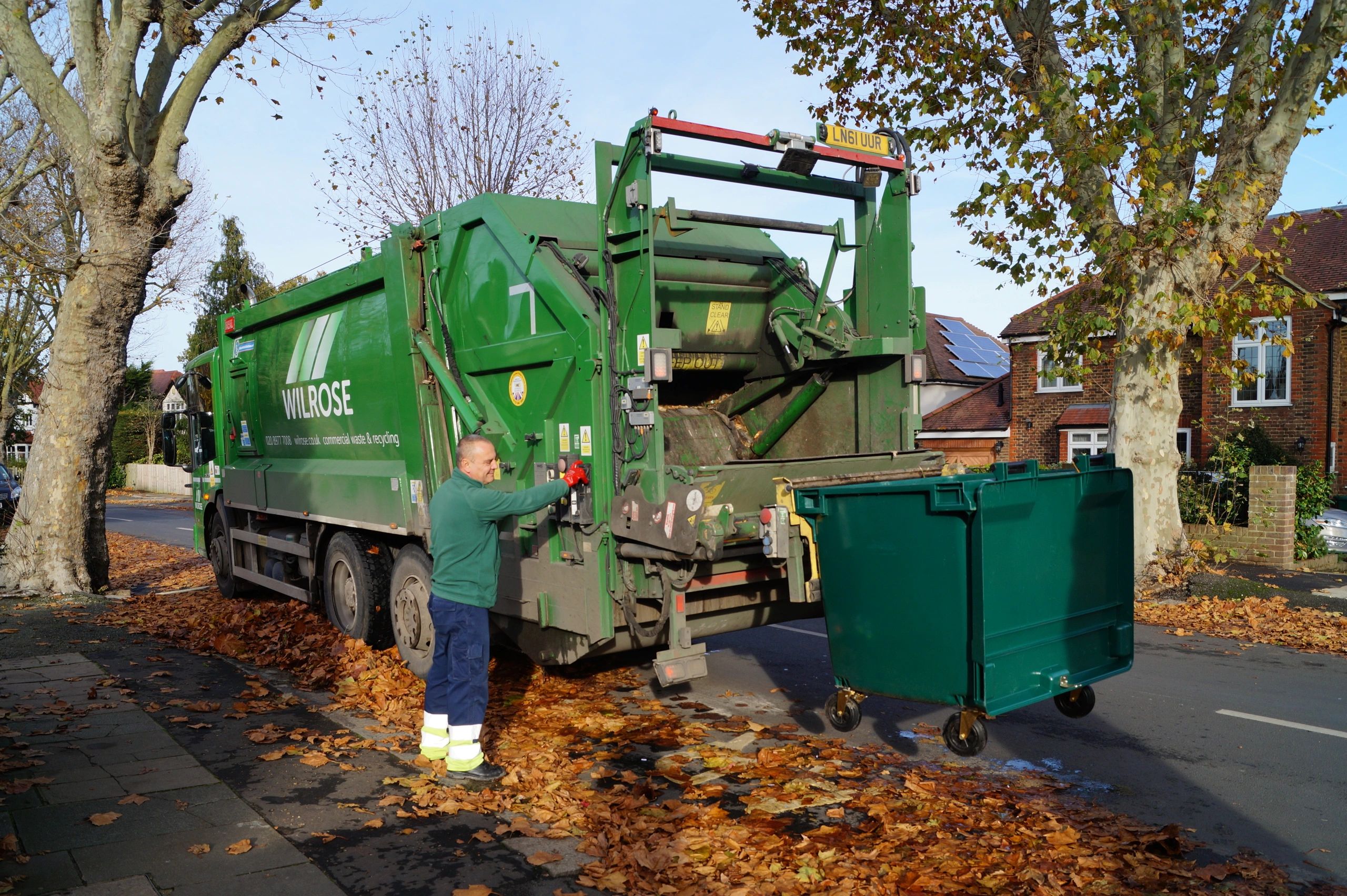 Dustcart ready for commercial waste service collection. Man standing next to vehicle.