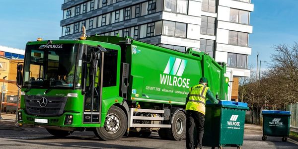 commercial waste dustcart with operative pushing wheelie bin to rear of vehicle.