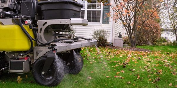 Lawn care machine spraying water on grass with autumn leaves around.