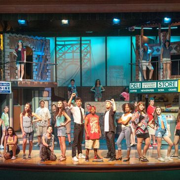 Group of actors performing on stage with urban backdrop.
