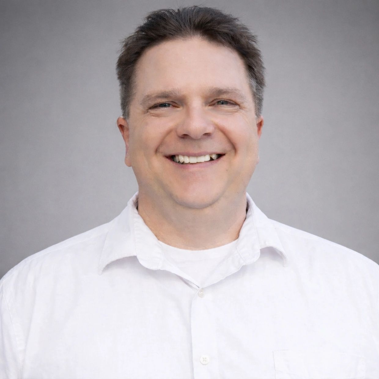 Smiling man in a white shirt against a gray background.