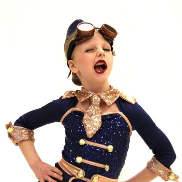A young girl in a sparkly navy and gold costume with goggles strikes a confident pose.