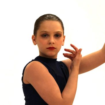 Young dancer posing with focused expression in a dark outfit.